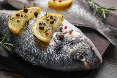 Photo of Fresh dorado fish, lemon slices and peppercorns on dark board, closeup