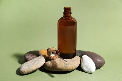 Bottle of face serum and dropper on spa stones against light green background