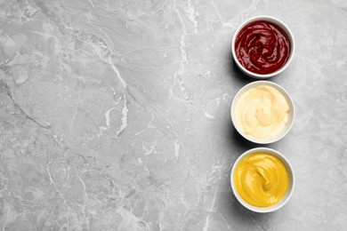 Bowls with mustard, ketchup and mayonnaise on light grey table, flat lay. Space for text
