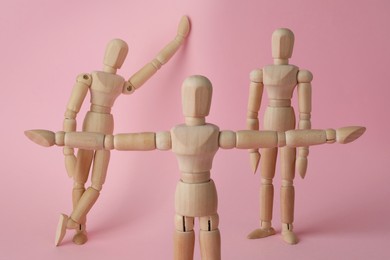 Wooden human models in different poses on pink background