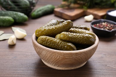 Photo of Bowl of pickled cucumbers and ingredients for food preservation on wooden table, closeup