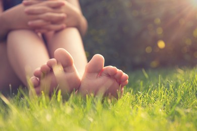 Photo of Teenage girl sitting barefoot on green grass outdoors, closeup. Space for text