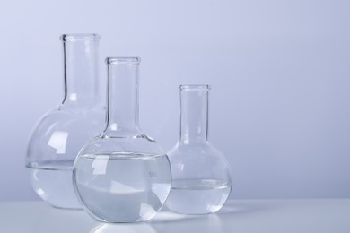 Florence flasks with transparent liquid on table against light background. Space for text