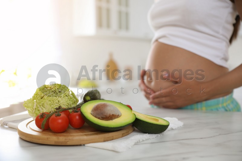 Fresh vegetables at table and young pregnant woman in kitchen, closeup. Taking care of baby health