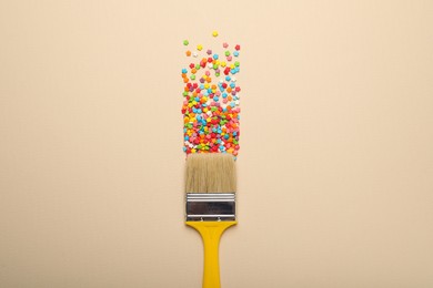 Photo of Brush painting with colorful sprinkles on beige background, top view. Creative concept
