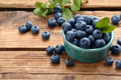 Tasty fresh blueberries and green leaves on wooden table, space for text