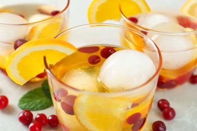 Delicious cocktails with orange, cranberries and ice balls on light grey marble table, closeup