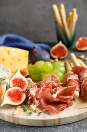Photo of Board with delicious figs, cheese, grapes and bread with proscuitto on grey table, closeup