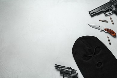 Photo of Flat lay composition with balaclava and weapons on light grey table, space for text
