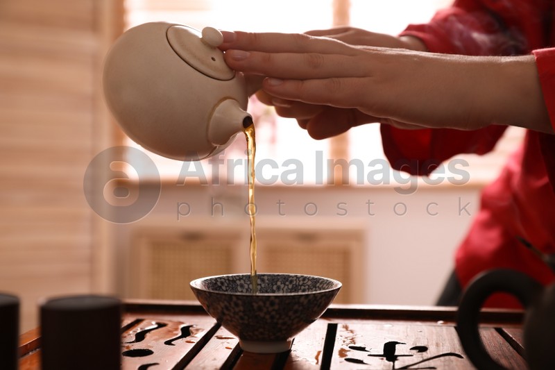 Master pouring freshly brewed tea into cup during traditional ceremony at table, closeup