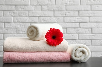 Rolled and folded soft towels with flower on table near brick wall