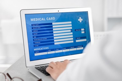 Photo of Doctor using laptop to fill out patient's medical card at table in clinic, closeup