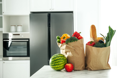 Paper bags with fresh products on table near modern refrigerator in kitchen