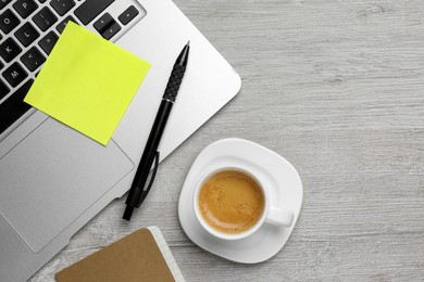 Laptop with blank sticky note, pen and cup of coffee  on white wooden table, flat lay. Space for text