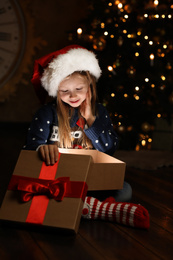 Cute child opening magic gift box near Christmas tree at night