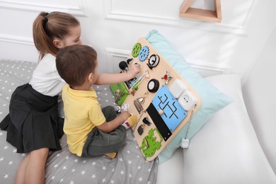 Little boy and girl playing with busy board on bed in room