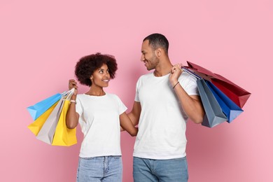 Photo of Happy African American couple with shopping bags on pink background