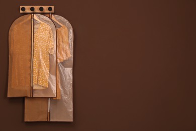 Garment bags with clothes hanging on brown wall. Space for text