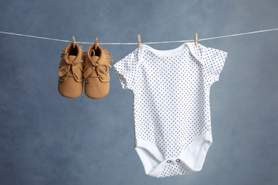 Photo of Child's bodysuit, pair of booties hanging on laundry line against dark background