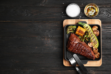 Delicious beef tenderloin served on black wooden table, flat lay. Space for text