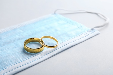 Wedding rings and medical mask on grey background, space for text. Divorce during coronavirus outbreak