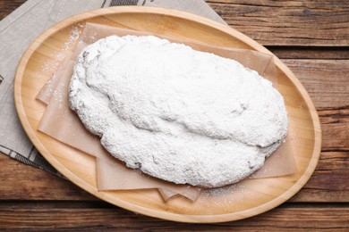 Plate of delicious Stollen sprinkled with powdered sugar on wooden table, top view
