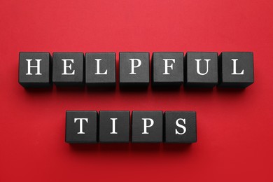 Photo of Phrase Helpful Tips made of black cubes with letters on red background, top view