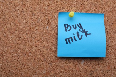 Photo of Light blue paper note with phrase Buy Milk on cork board, closeup. Space for text