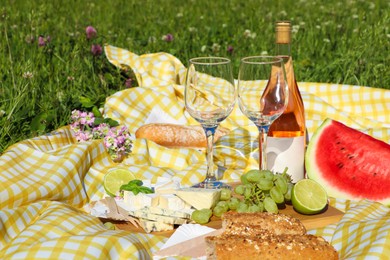 Picnic blanket with delicious food and wine on green grass outdoors