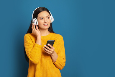 Young woman listening to audiobook on blue background. Space for text