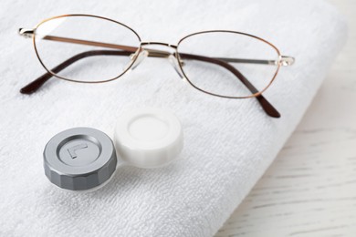 Photo of Case with contact lenses, glasses and towel on white wooden table, closeup