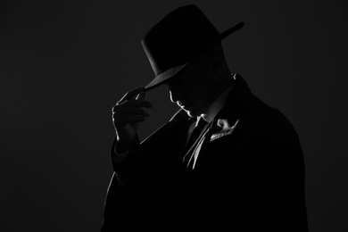 Old fashioned detective in hat on dark background, black and white effect