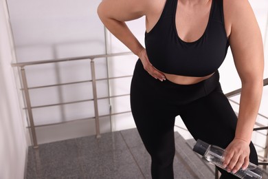 Overweight woman suffering from pain in right side on stairs indoors, closeup. Space for text