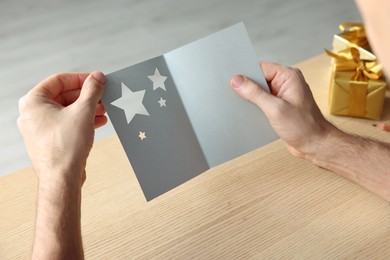 Photo of Man holding greeting card at wooden table, closeup