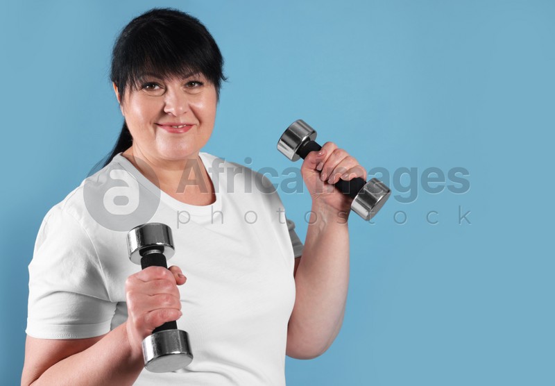 Photo of Happy overweight mature woman doing exercise with dumbbells on light blue background