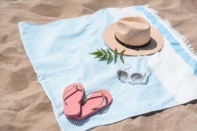 Photo of Beach towel with straw hat, sunglasses, leaves and flip flops on sand