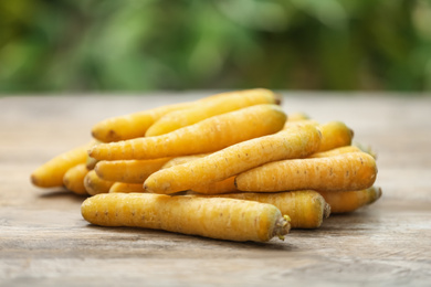 Raw yellow carrots on wooden table against blurred background
