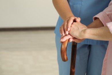 Elderly woman with walking cane and female caregiver indoors, closeup. Space for text