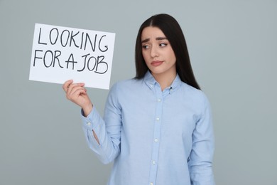 Photo of Young unemployed woman holding sign with phrase Looking For A Job on grey background