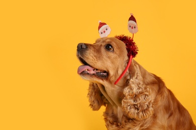 Adorable Cocker Spaniel dog in Santa headband on yellow background, space for text