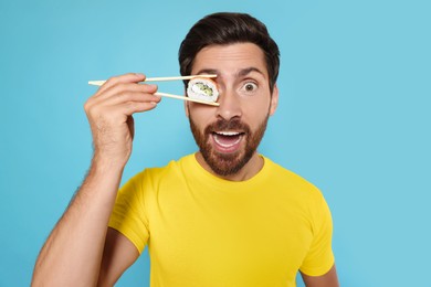 Photo of Funny man hiding his eye with tasty sushi roll on light blue background