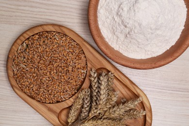 Photo of Wheat grains, flour and spikelets on wooden table, flat lay