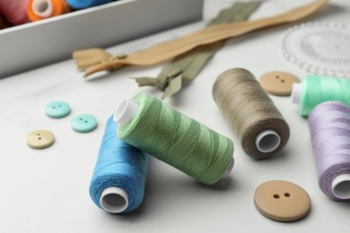 Sewing threads and buttons on white marble table, closeup