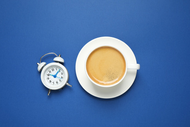 Classic black coffee and alarm clock on blue background, top view. Color of the year 2020