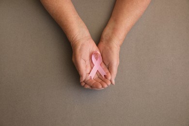Senior woman holding pink ribbon on grey background, top view. Breast cancer awareness