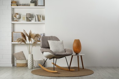 Soft rocking chair with pillow on rug near wall in room. Interior design