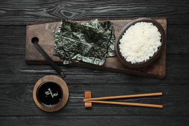 Dry nori sheets, rice, soy sauce and chopsticks on black wooden table, flat lay