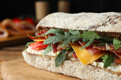 Delicious sandwich with fresh vegetables and prosciutto on wooden table, closeup