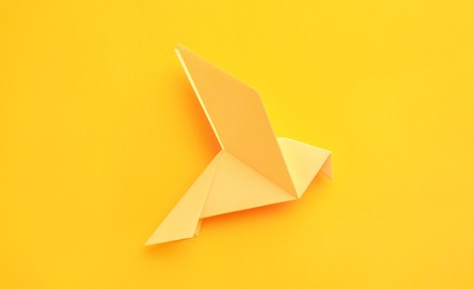 Photo of Origami art. Beautiful handmade paper bird on yellow background, top view