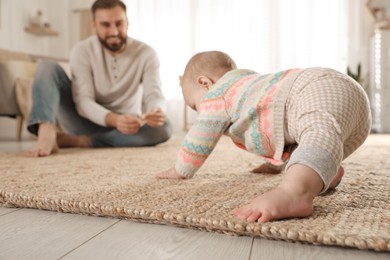 Happy young father watching his cute baby crawl on floor at home